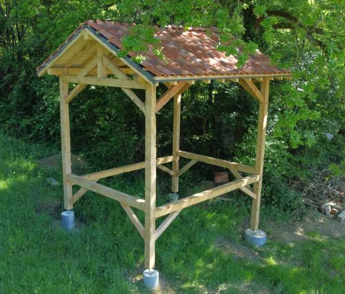 Cabane sur pilotis en bois massif, à structure traditionnelle et toit en tuiles, construite dans un cadre naturel verdoyant.