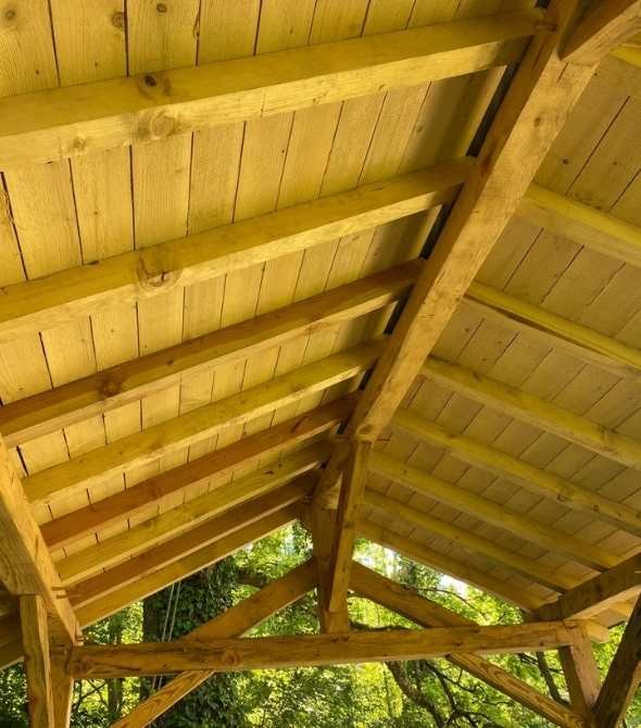 Vue intérieure de la toiture en bois d’une cabane sur pilotis, montrant la charpente traditionnelle et les assemblages artisanaux en bois massif.