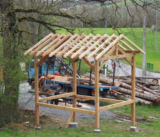 Charpente en bois d’une cabane en construction, réalisée artisanalement par un charpentier, utilisant du bois local pour une structure solide et durable.