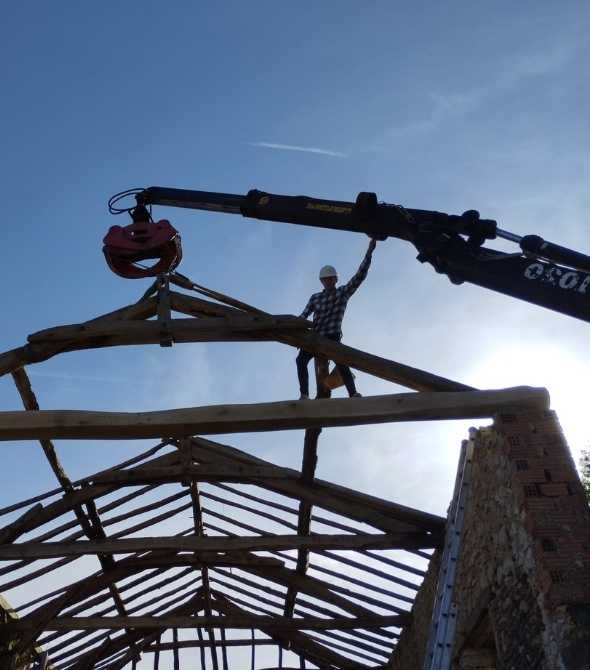 Charpentier posant une charpente traditionnelle en bois massif à l’aide d’une grue sur un bâtiment ancien en rénovation