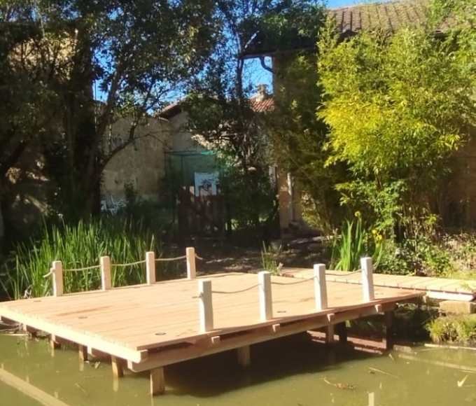 Ponton en bois construit sur pilotis au bord d’un plan d’eau, réalisé avec une structure robuste et harmonieuse, intégrée dans un environnement végétalisé.